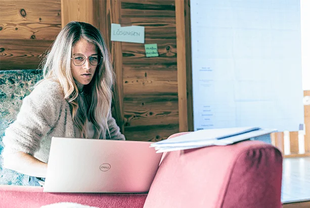 Frau sitzt auf der Kante eines Sessels und schaut auf ihren Laptop