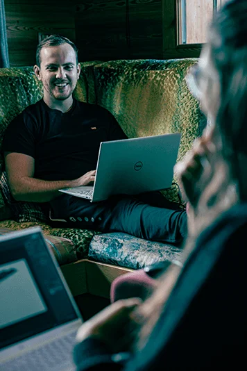 Mitarbeiter sitzen sich gegenüber & arbeiten lachend an ihren Laptops